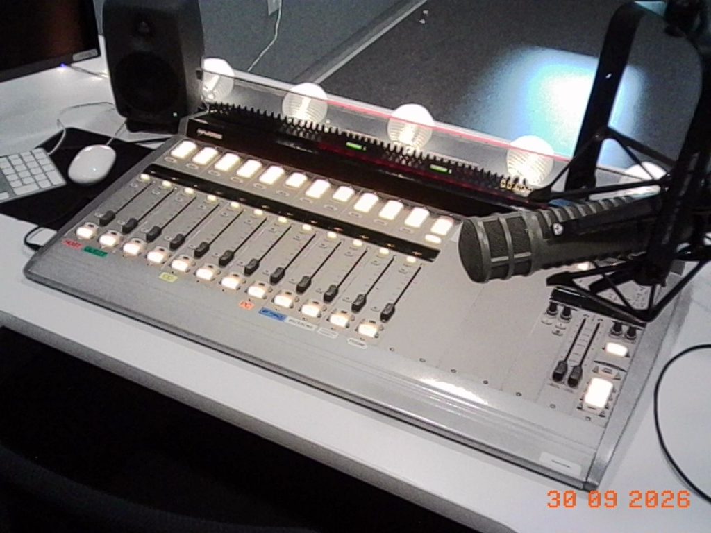 "Audio Mixer"
A large rectangular gray audio mixer with lit up string lights behind it and a microphone in the top right corner.