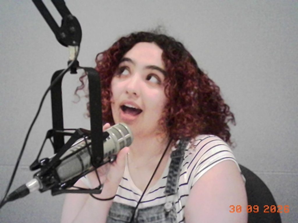 "Sofia in Studio"
Blog post author Sofia holding the microphone and wearing headphones while looking upwards towards the left.